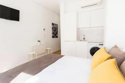 a white bedroom with a large bed and a kitchen at Downtown Porto Mouzinho Studio Apts in Porto