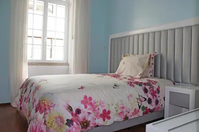 a bedroom with a bed with a floral comforter and a window at Grande Oceano Guest House in Porto