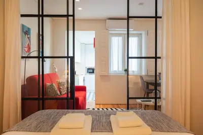 a room with a bed and a red chair and a table at Modern loft w AC Downtown and Metro in Porto