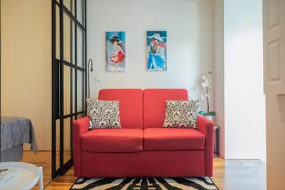 a red chair in a living room with paintings on the wall at Modern loft w AC Downtown and Metro in Porto