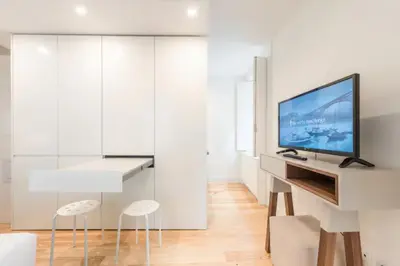 a white living room with a tv and two stools at GuestReady - The New Yellow Ledbetter in Porto