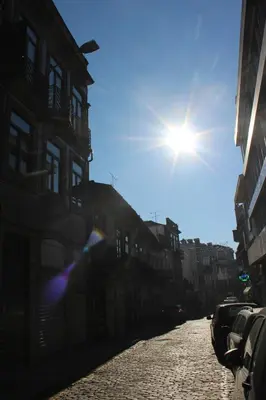 a sun shining on a cobblestone street with buildings at Bonjardim Flats - T1 com varanda in Porto