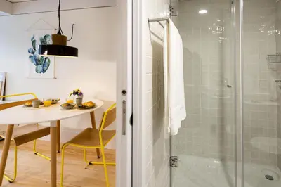 a bathroom with a glass shower and a table and chair at Studio Tomás Gonzaga in Porto