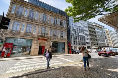 two people crossing a street in front of a building at Merc Porto Bolhão Place in Porto