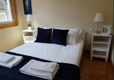 a bedroom with a bed with white sheets and blue pillows at Cosy Santa Catarina Flat in Porto