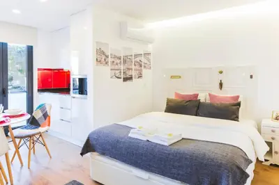a white bedroom with a large bed and a kitchen at APOSENTUS - Your Home at Pinheiro's Studio in Porto