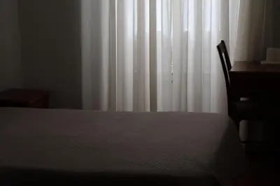 a bedroom with a bed and a desk and a white curtain at Hotel Peninsular- Porto in Porto