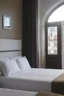 a bed with white pillows in a room with a window at Hotel Chique Aliados in Porto