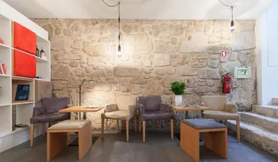 a room with tables and chairs and a stone wall at InPatio Guest House in Porto