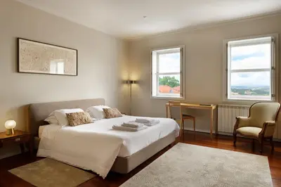 a bedroom with a bed and a chair and two windows at Casas Da Formiga - Riverview Terrace and Pool in Porto