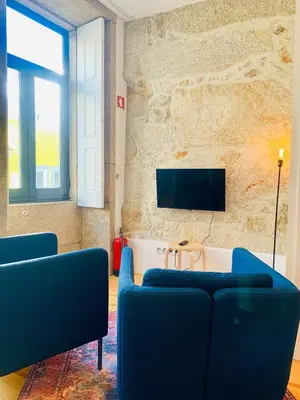 a living room with two blue chairs and a tv on a stone wall at Oporto Chic&Cozy - Santo Ildefonso in Porto
