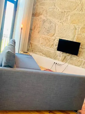 a couch in front of a stone wall with a television at Oporto Chic&Cozy - Santo Ildefonso in Porto