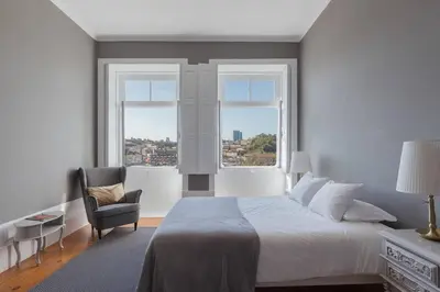 a bedroom with a bed and a chair and two windows at GuestReady - Innvict Residences in Porto