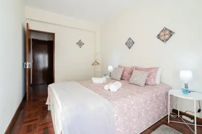 a white bedroom with a large bed with pink sheets at Cozy Apartment Alegria Balcony in Porto
