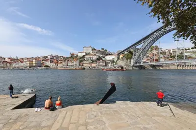 a group of people sitting on the banks of a river with a bridge at FLH Living Oporto Lofts in Porto
