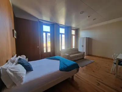 a bedroom with a bed and a chair and windows at Loulé Estúdios in Porto