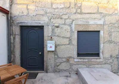 a stone building with a black door and two windows at A Ilha do Lindo Vale in Porto