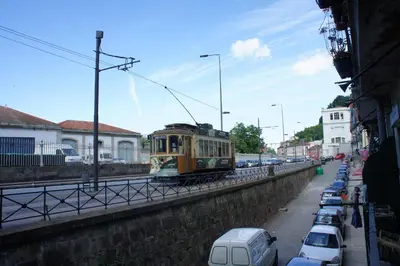 a trolley car driving down a street with parked cars at Alfandega Apartments in Porto