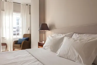 a bedroom with a white bed with a chair and a window at B The Guest Downtown in Porto