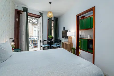 a bedroom with a bed and a kitchen with green cabinets at Renovated Feb25 Clerigos Cozy Balcony with self check in in Porto