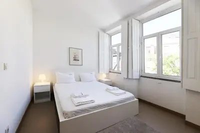 a white bedroom with a bed with two windows at FLH Porto City Apartment with Balcony in Porto