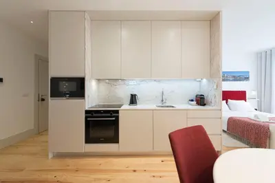 a kitchen with white cabinets and a red chair at Heart of D Pedro Apartments in Porto