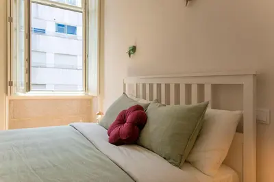 a bed with a red pillow on it with a window at LovelyStay - 2BR Flat with AC in Duque de Loulé in Porto
