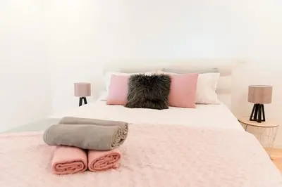 a white bed with pink and grey pillows on it at Porto Wine Loft Duplex with swimming pool in Vila Nova de Gaia