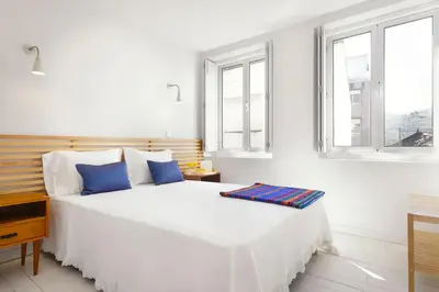 a white bedroom with a large bed with blue pillows at O´Porto Outeiro Flat in Porto