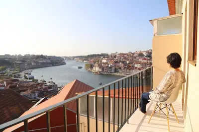 a woman sitting on a chair on a balcony looking at a river at Casa do Pilar - D Maria Pia in Vila Nova de Gaia