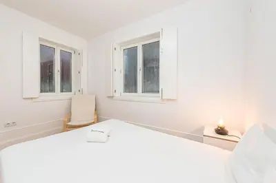 a white bedroom with a bed and two windows at GuestReady - Triple C's in Porto