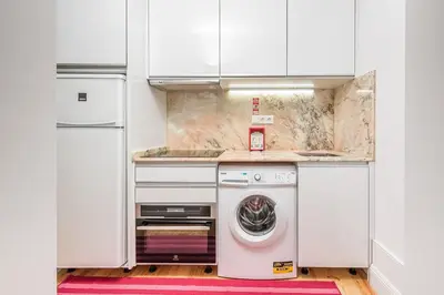 a kitchen with white cabinets and a washer and dryer at GuestReady - Triple C's in Porto