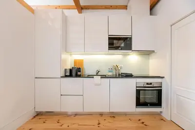 a white kitchen with white cabinets and a wooden floor at Newly Renovated Cozy Central Loft w/ AC by LovelyStay in Porto
