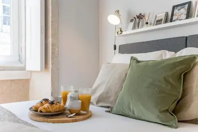 a tray of food on a bed with two glasses of orange juice at Mouzinho Darling 1BR w/ AC in City Center by LovelyStay in Porto