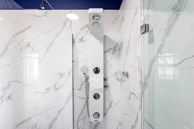 a bathroom with a shower with white marble walls at Mouzinho Darling 1BR w/ AC in City Center by LovelyStay in Porto