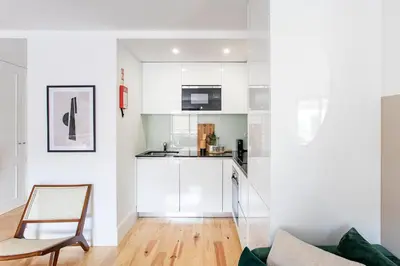 a kitchen with white cabinets and a chair in a room at Bright 3BR Flat w/ AC in City Center by LovelyStay in Porto
