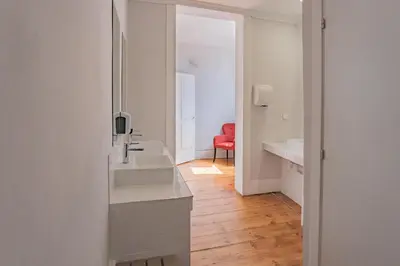 a white bathroom with a sink and a red chair at Rosalma Hostel in Porto