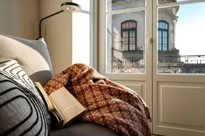 a book and a blanket on a couch with a window at Liberty 119 • Luxurious 1BD in Porto's main Avenue in Porto