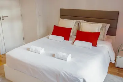 a large white bed with red pillows on it at Apartamento Luminoso no Centro in Porto
