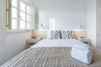 a white bedroom with a large bed and two windows at GuestReady - Port Studio 2 in Vila Nova de Gaia