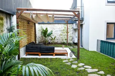 a patio with a black couch under a pergola at Lindo apartamento 2 quartos com pátio - Batalha - APT C in Porto