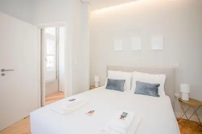 a white bedroom with a large white bed with two blue pillows at Liiiving in Porto - Aliados Stone Apartment in Porto