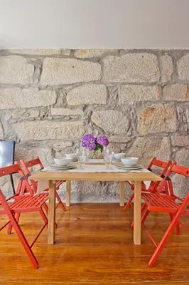 a wooden table with two red chairs and a stone wall at Porto Sé Apartamentos in Porto