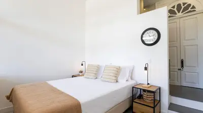 a bedroom with a white bed with a clock on the wall at OPOrto Downtown Studio by LovelyStay in Porto