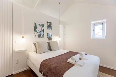 a white bedroom with a bed with two towels on it at Wonderful 2BR Duplex Near River by LovelyStay in Porto