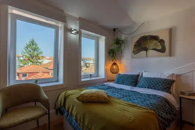 a bedroom with a bed with a chair and two windows at OPO Alegria 119 in Porto