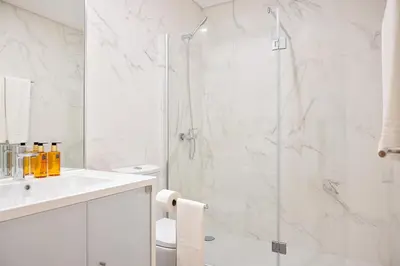 a white bathroom with a shower and a sink at Palmeiras Apartment, by Bolhão Residences in Porto