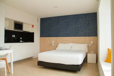a bedroom with a white bed and a desk and a kitchen at room Select Porto Suites in Porto