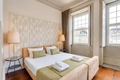 a bedroom with a large white bed and two windows at Traça Apartments by DA'HOME in Porto