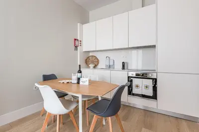 a kitchen with white cabinets and a wooden table and chairs at GuestReady - Bonjardim Building in Porto